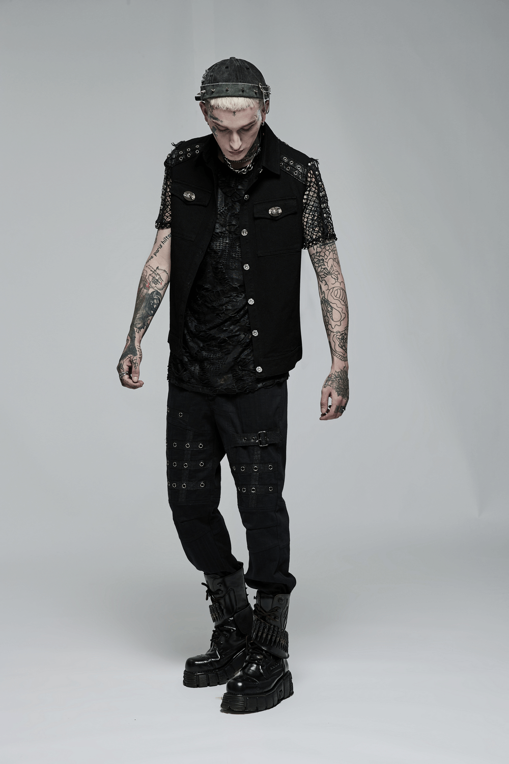 Edgy punk model wearing a sleeveless twill vest with studs, paired with dark pants and bold accessories.