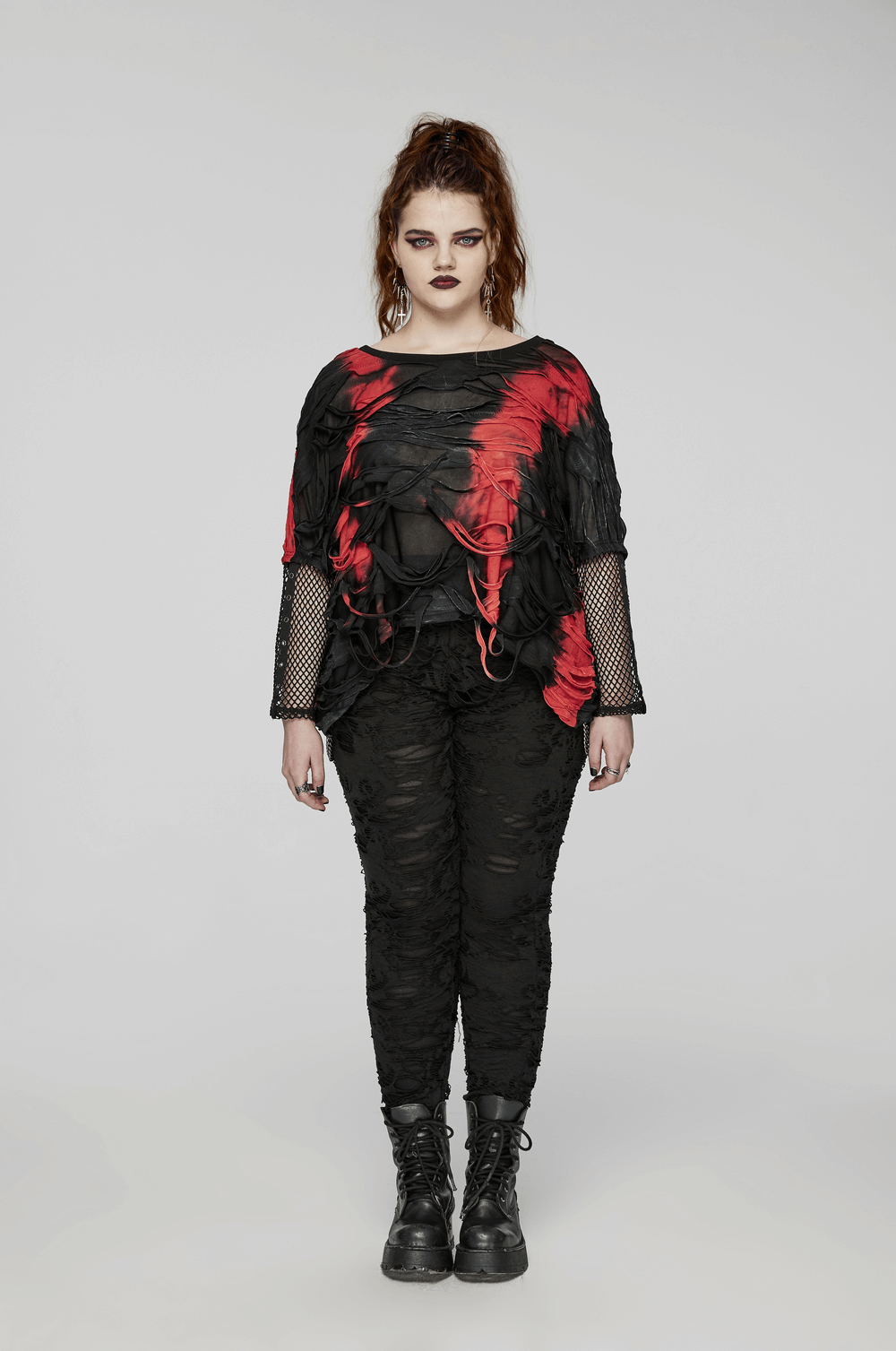 Edgy women’s punk tie-dye top with mesh sleeves in red and black, paired with shredded black pants and combat boots.