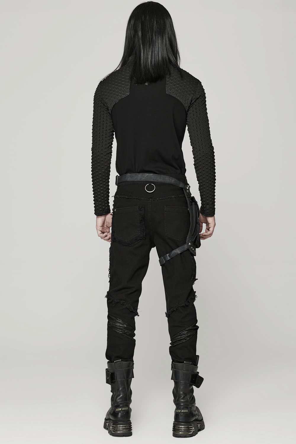Stylish individual in edgy punk outfit with unique back detailing and rugged pants, showcasing a bold fashion statement.