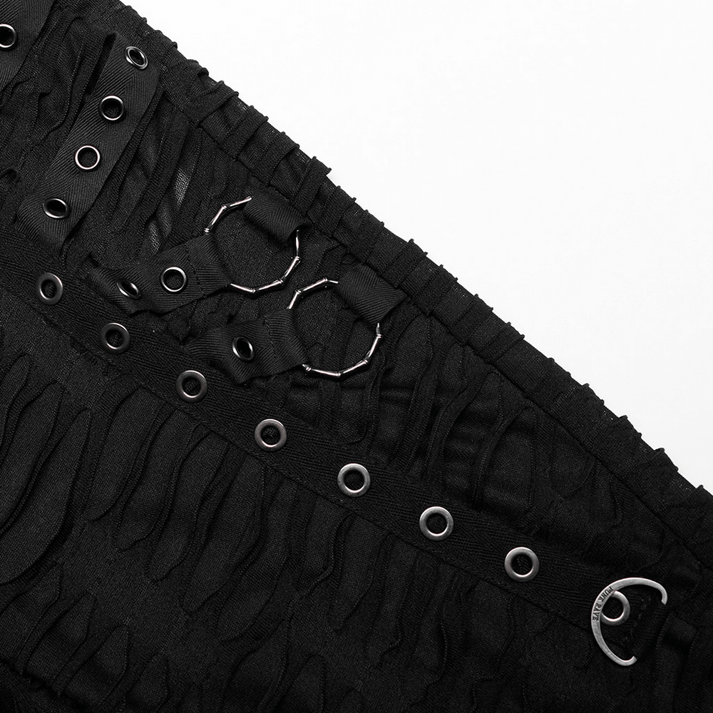 Close-up of edgy black leggings with ripped fabric, metal rivets, and rings showcasing bold goth style.