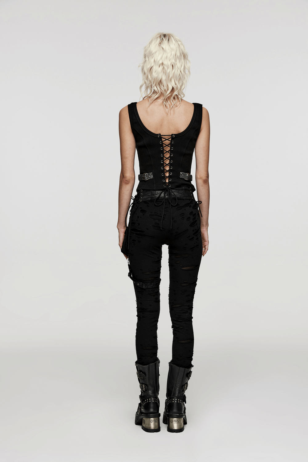 Back view of a stylish woman in a black lace-up top and distressed pants, showcasing edgy steampunk fashion.