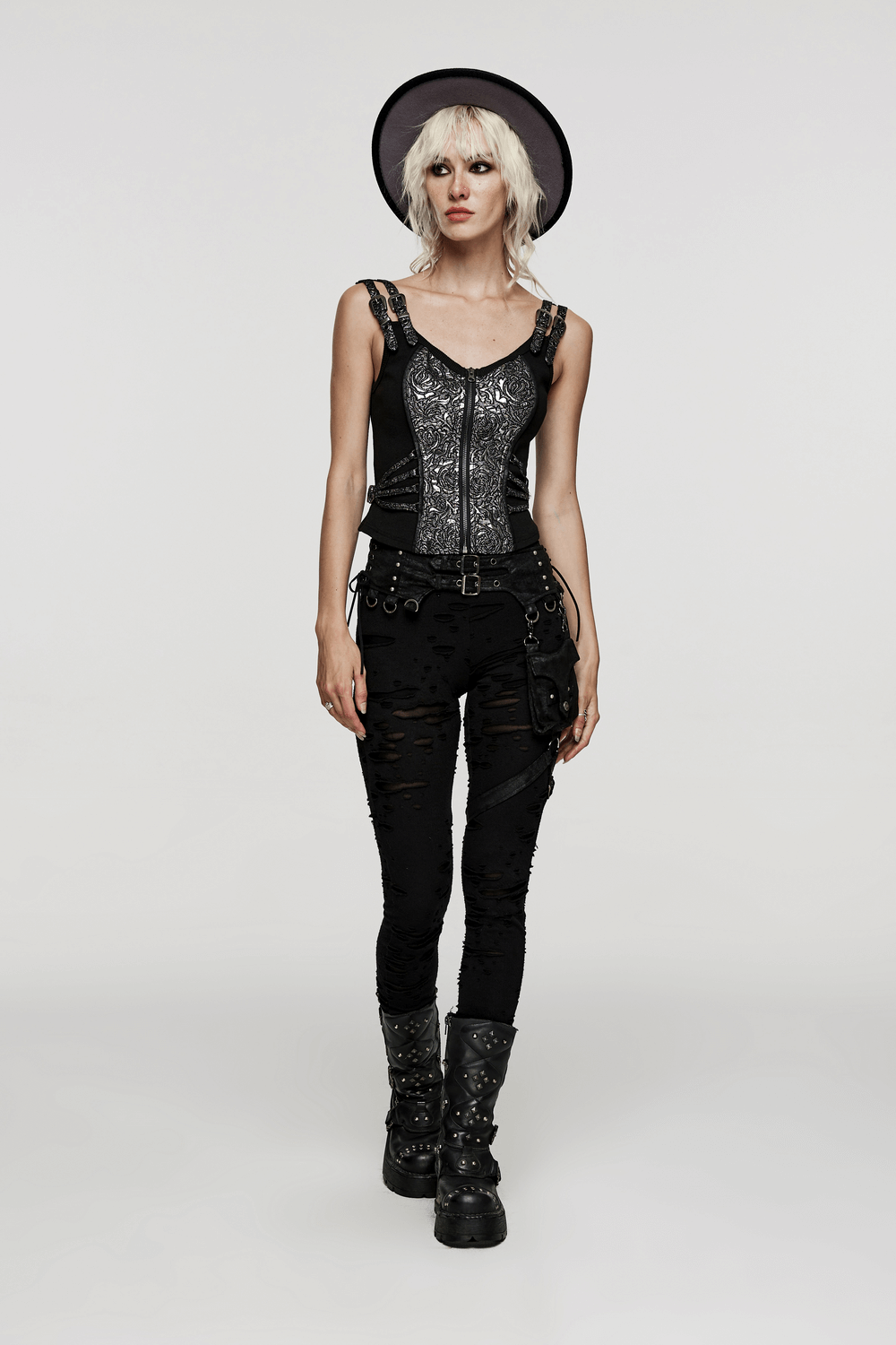 Edgy woman in a zippered steampunk jacquard waistcoat, distressed black pants, and stylish boots.