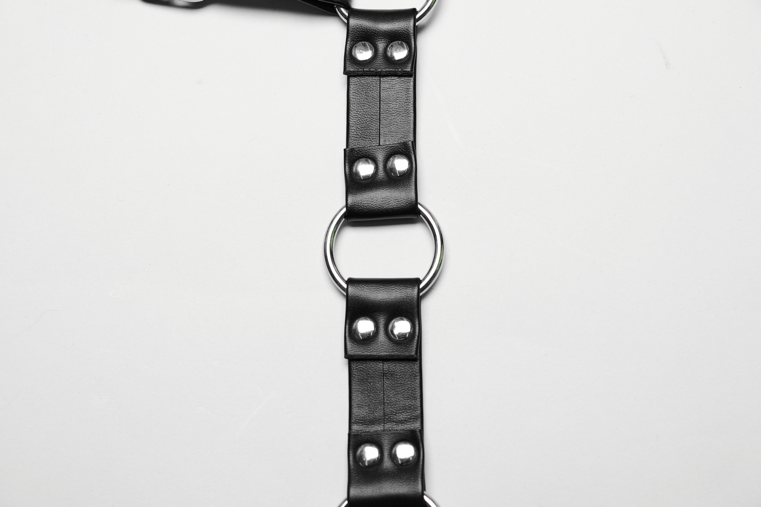 Close-up of a black PU leather body harness featuring metal rings and studs, designed for a bold punk style.