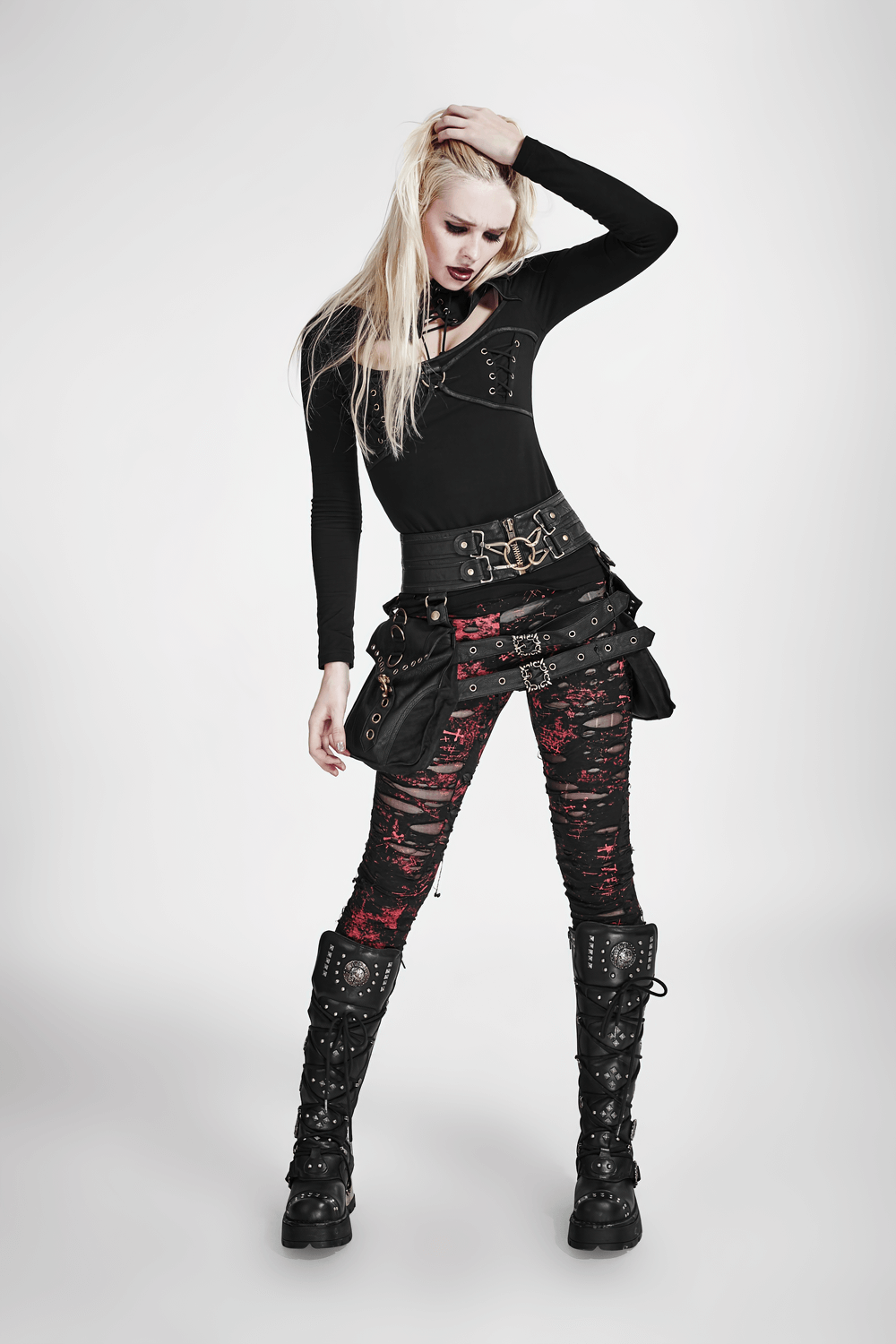 Edgy woman modeling shredded distressed punk rock leggings with a bold red underlay and black mesh accents.