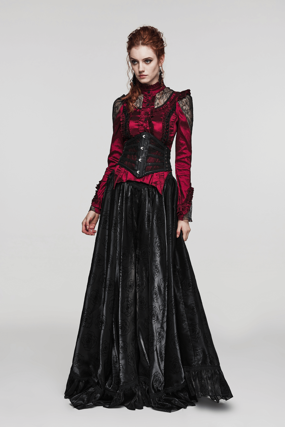 Model in elegant red and black gothic dress showcasing a corset and flowing skirt, embodying a dramatic punk style.