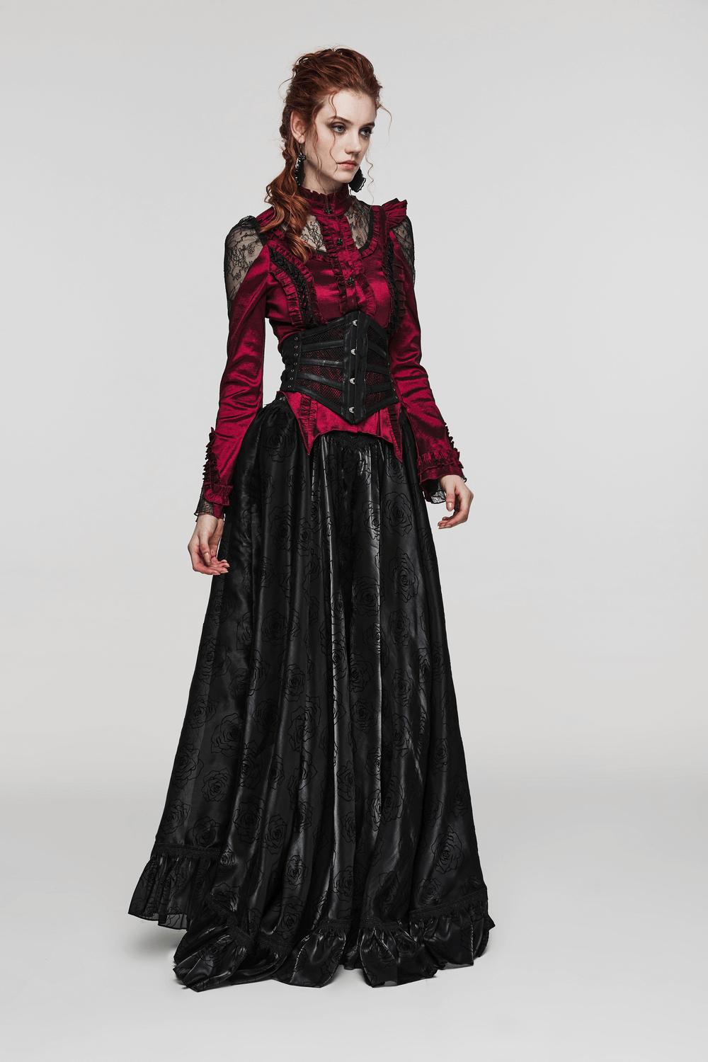 Model in a gothic red dress with black corset and flowing skirt, showcasing a dramatic punk fashion style.