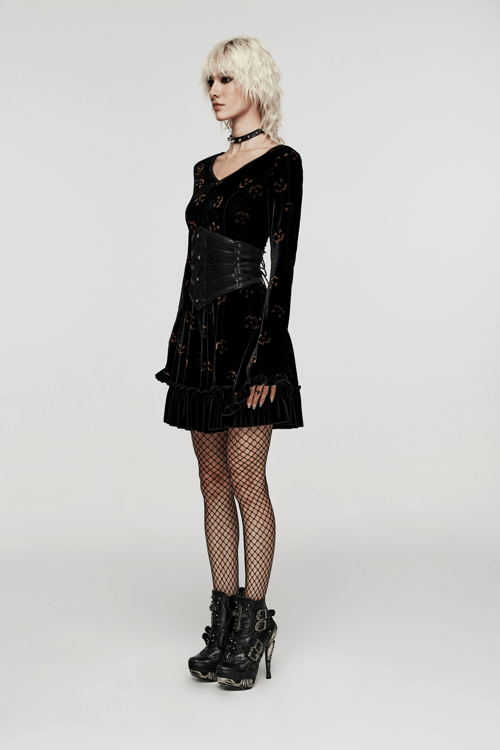 Model in a black velvet dress with a punk corset belt, fishnet stockings, and stylish ankle boots.