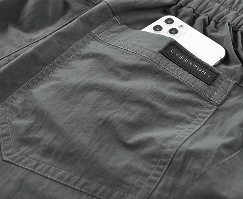 Close-up of elastic waist tactical shorts featuring a zippered pocket and a smartphone peeking out.