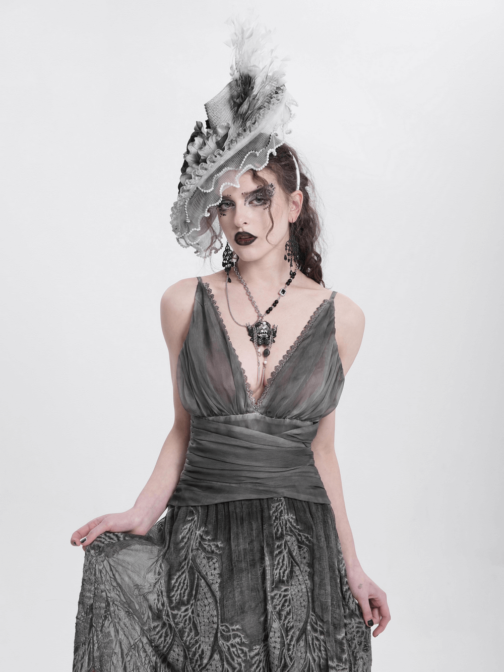 Elegant gothic model in grey dress wearing a black and white floral fascinator hat with feathers.