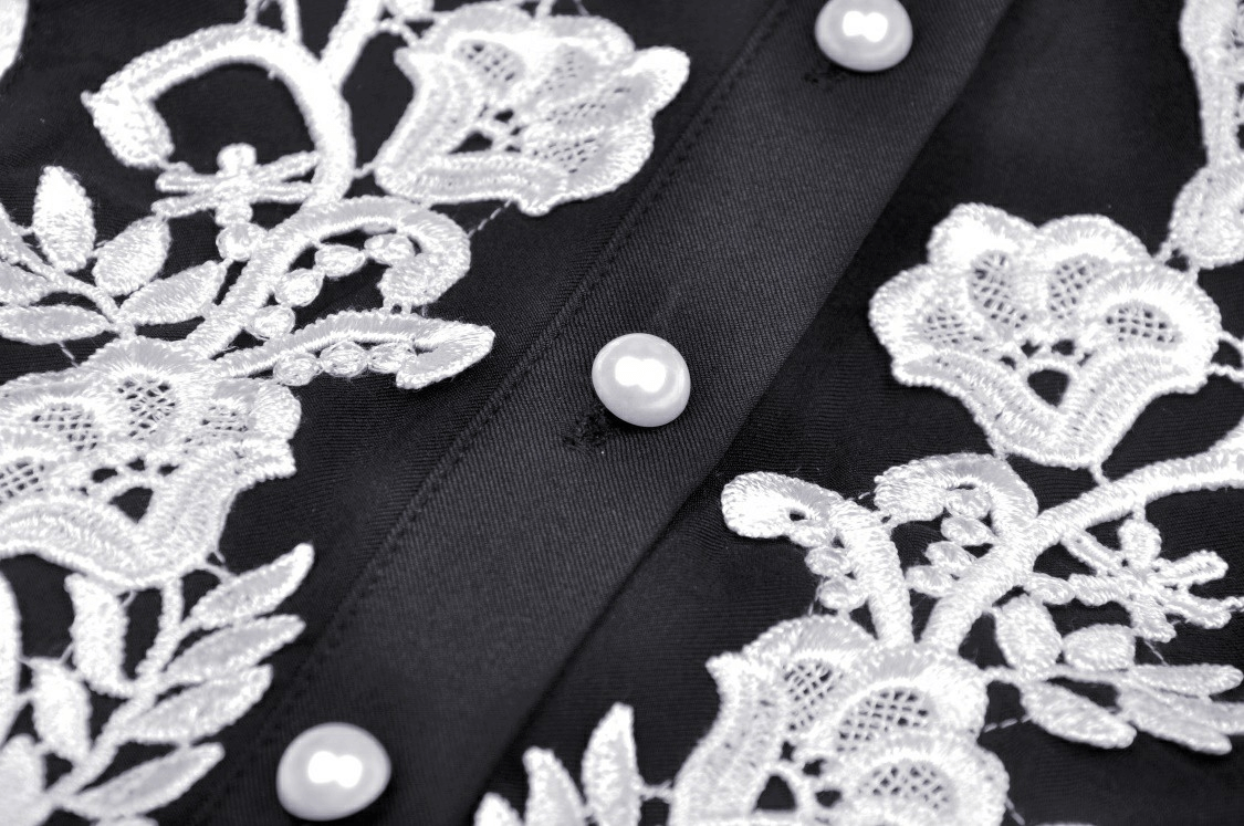 Close-up of intricate white floral embroidery on a chic black dress with buttons and a Peter Pan collar.