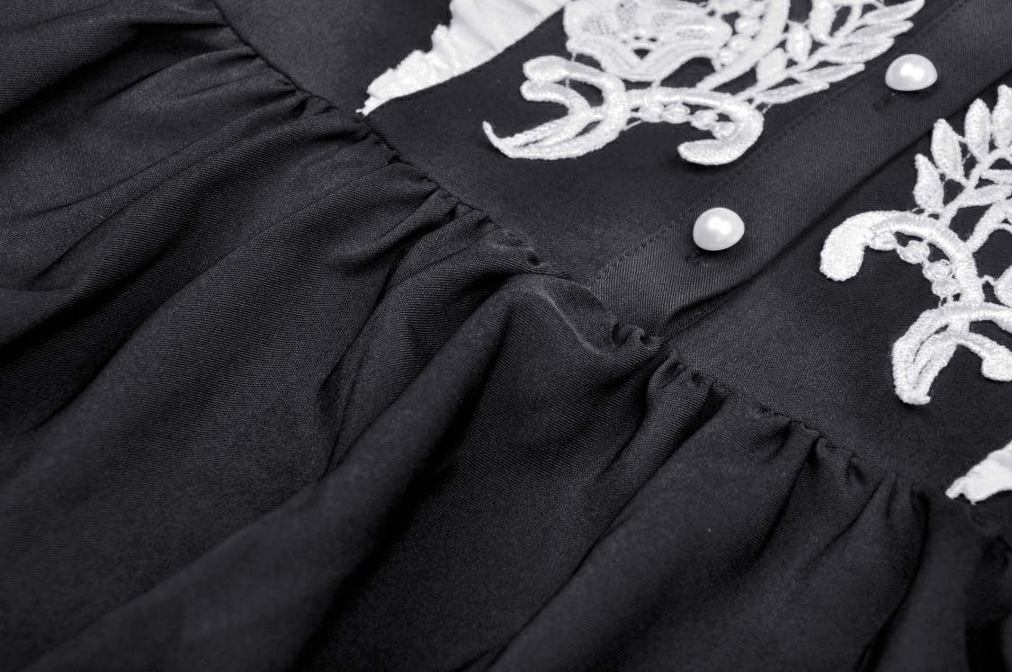 Close-up of the elegant black dress featuring intricate white floral embroidery and stylish buttons.