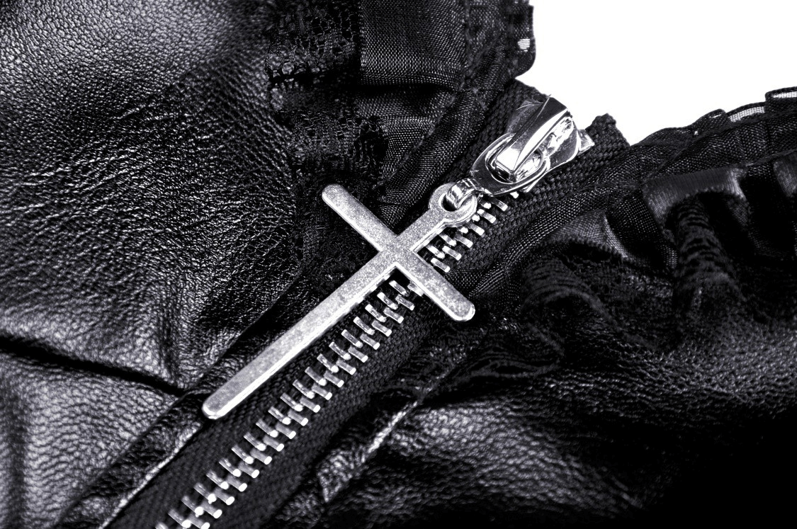 Close-up of zipper detail on a black leather dress with silver cross charm, showcasing stylish ruffle layers.