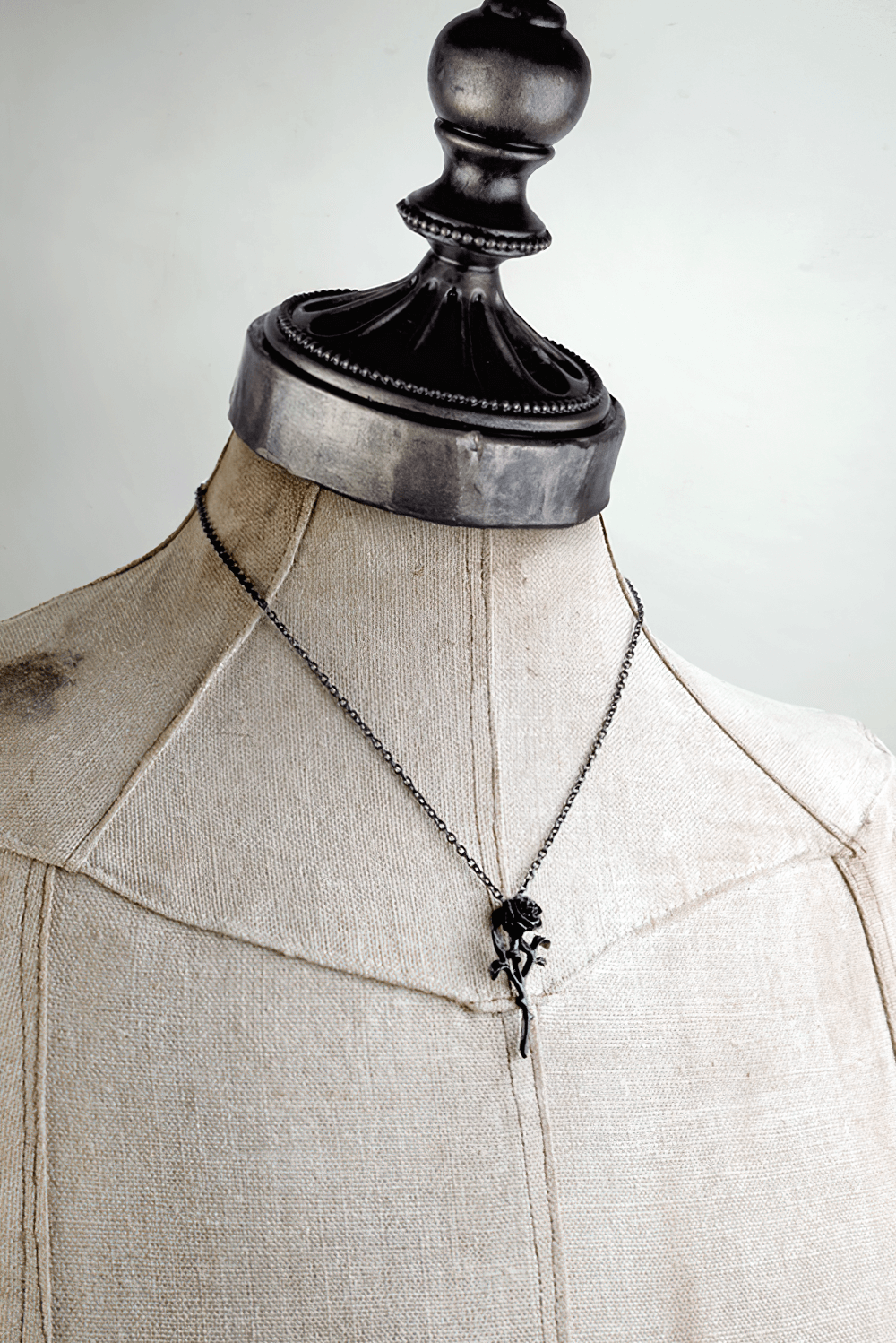 Elegant black rose gothic pendant necklace displayed on a vintage dress form, highlighting its antique finish.