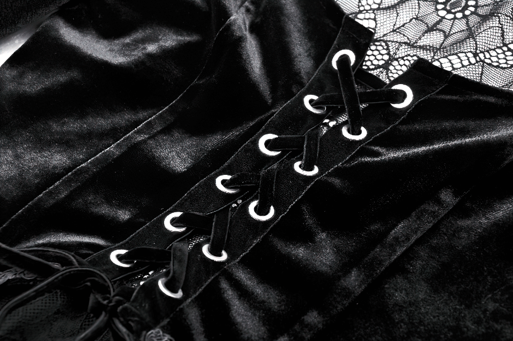 Close-up of an elegant black velvet lace-up dress with intricate lace detailing and bell sleeves.
