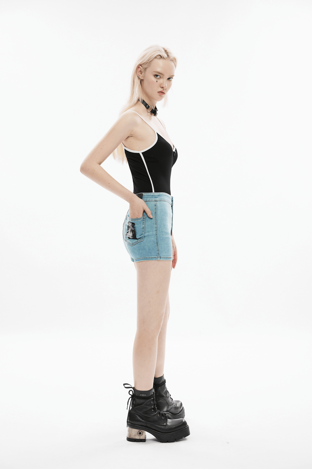 Side view of a model in a black and white camisole paired with denim shorts and platform boots.