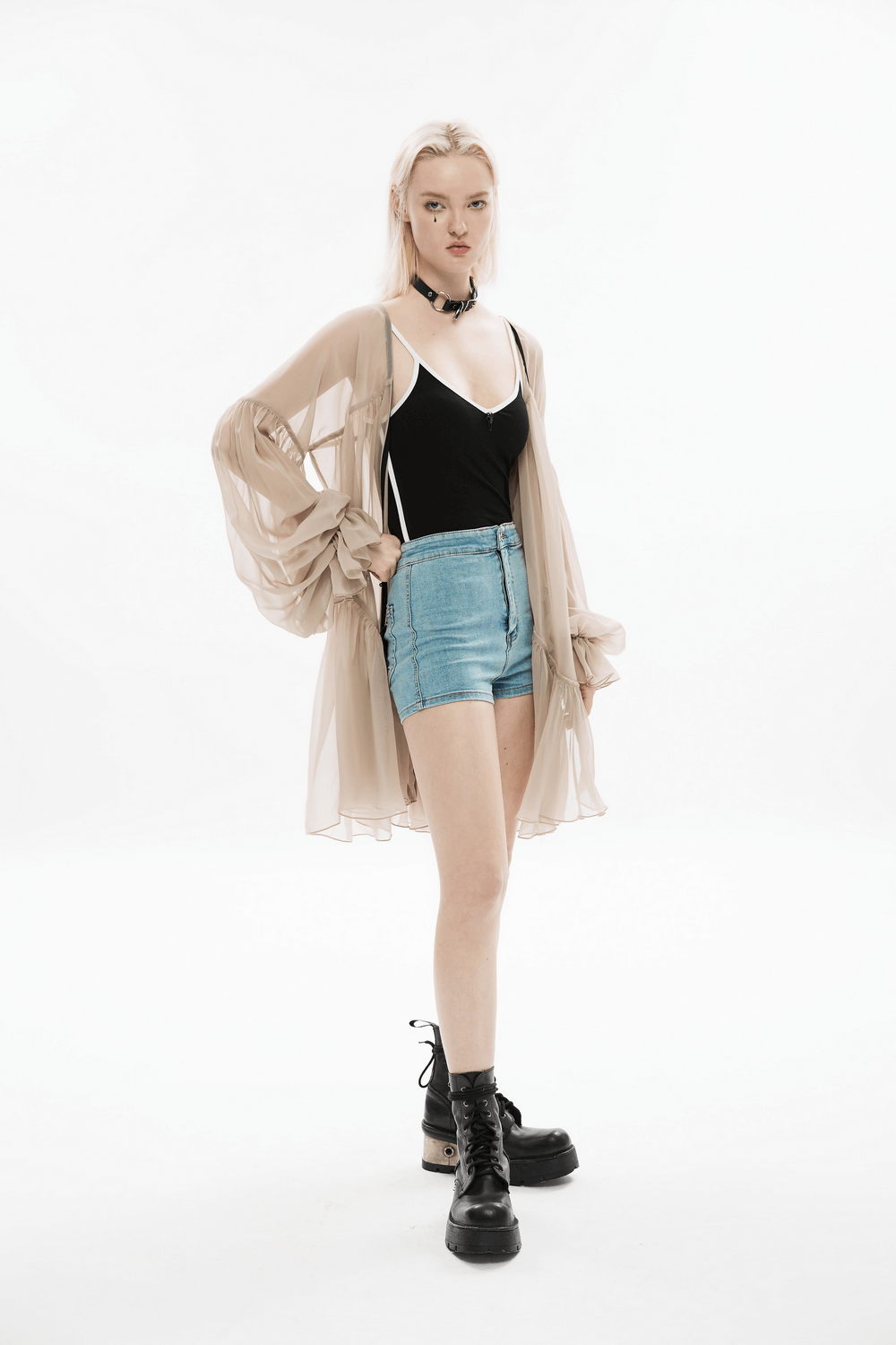 Chic model showcasing sheer beige kimono, black bodysuit, denim shorts, and edgy boots for a stylish look.