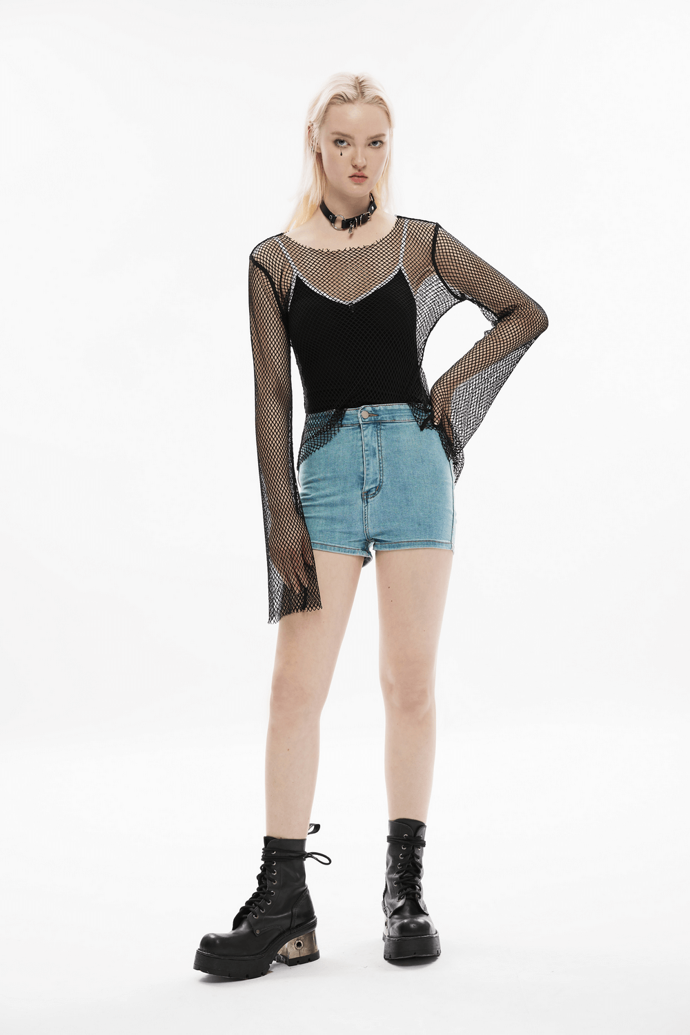 Model wearing a black mesh long-sleeve top and denim shorts, exuding edgy street style with combat boots.
