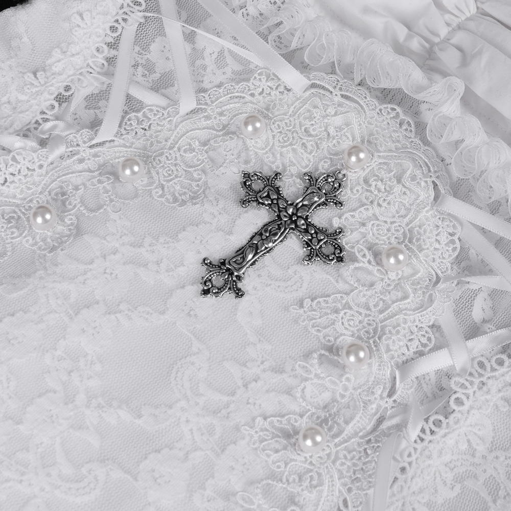 Detailed close-up of elegant white dress with lace, ruffle edges, pearls, and a decorative silver cross.
