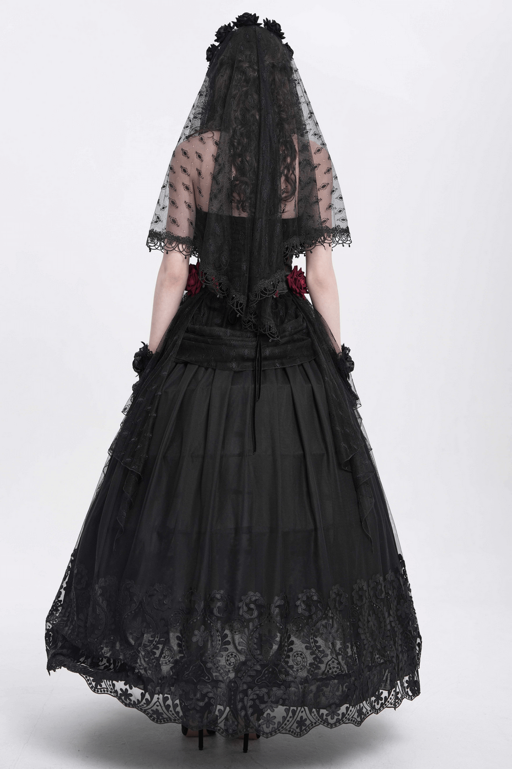 Back view of a woman in an elegant black mesh maxi skirt with floral embroidered hem and matching veil.