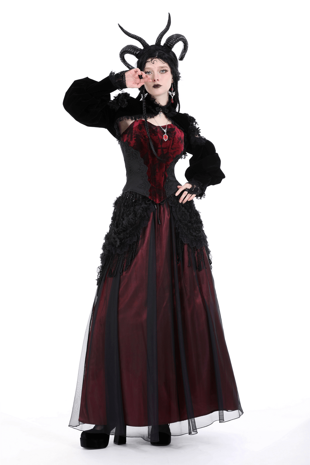 Elegant gothic model in black and red dress with lace accents and horns, showcasing a dramatic fashion statement.