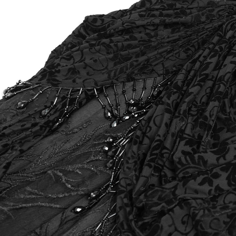 Close-up of elegant black velvet lace skirt with floral embroidery and draped beaded panels, showcasing gothic style.