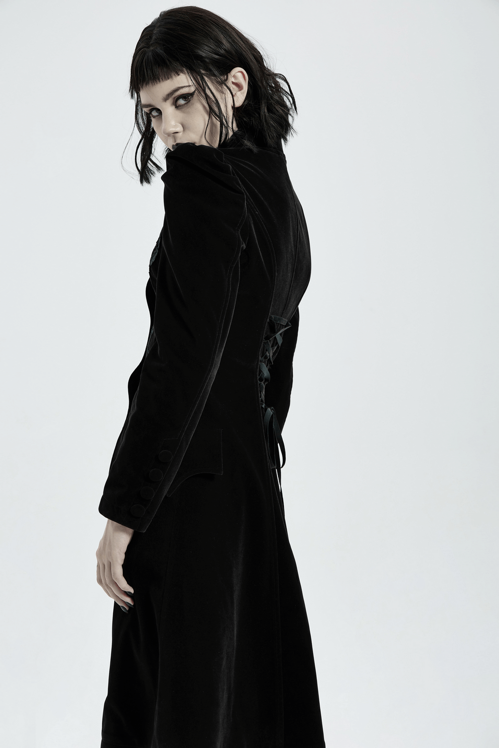 Stylish model showcasing Gothic black velvet lace-up trench coat, featuring dramatic lace-up back and slim fit design.