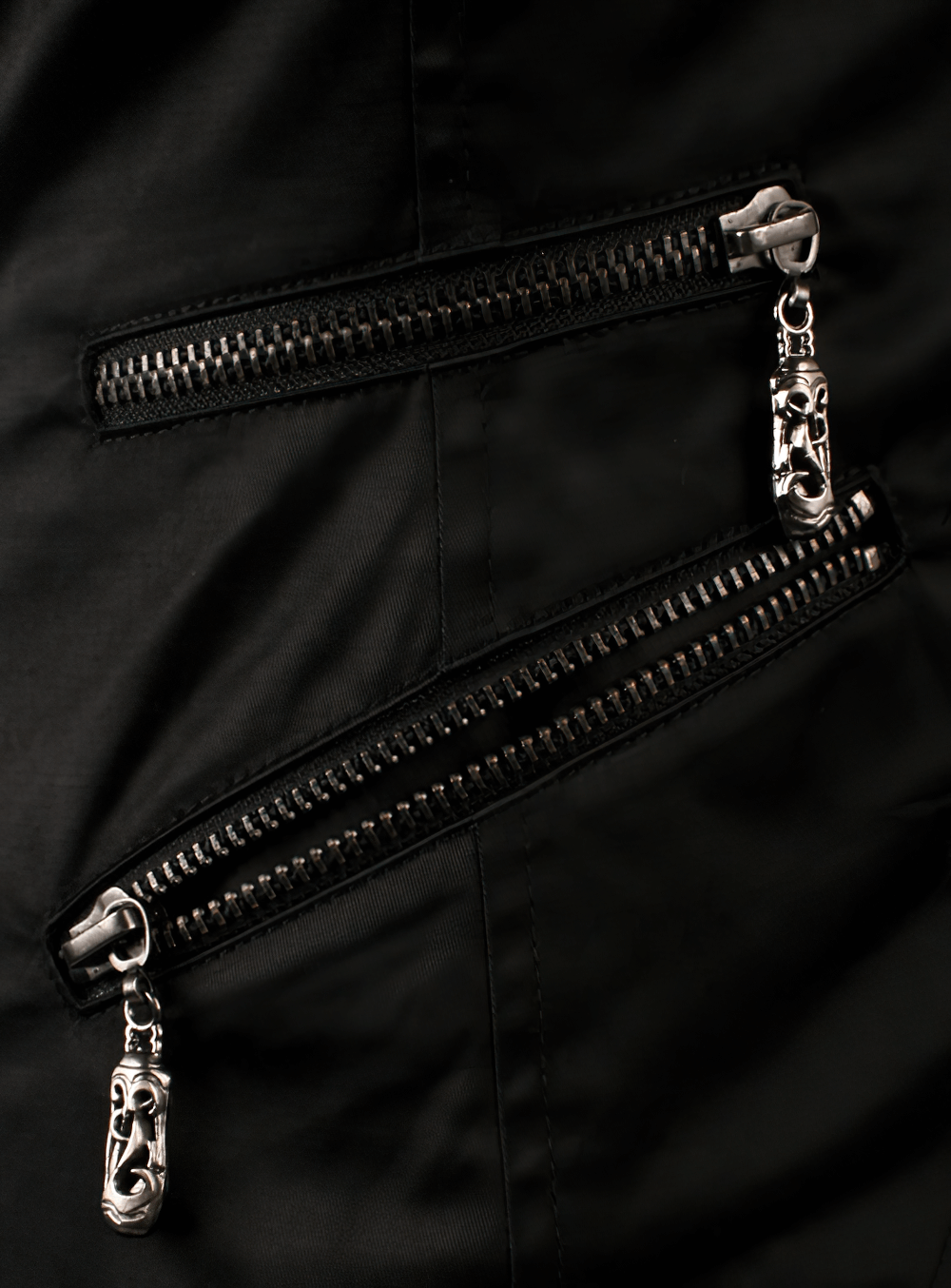 Close-up of unique silver zippers on a gothic black waistcoat, showcasing stylish asymmetrical design.