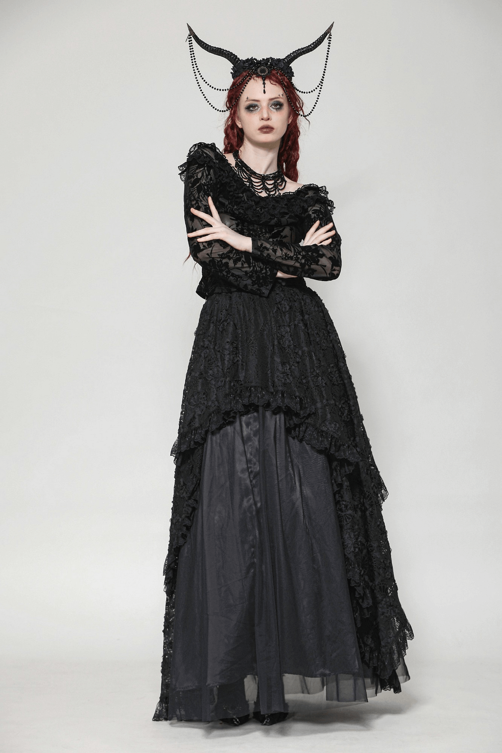 Gothic model wearing an elegant black lace dress with dramatic sleeves and a quirky horned headpiece.