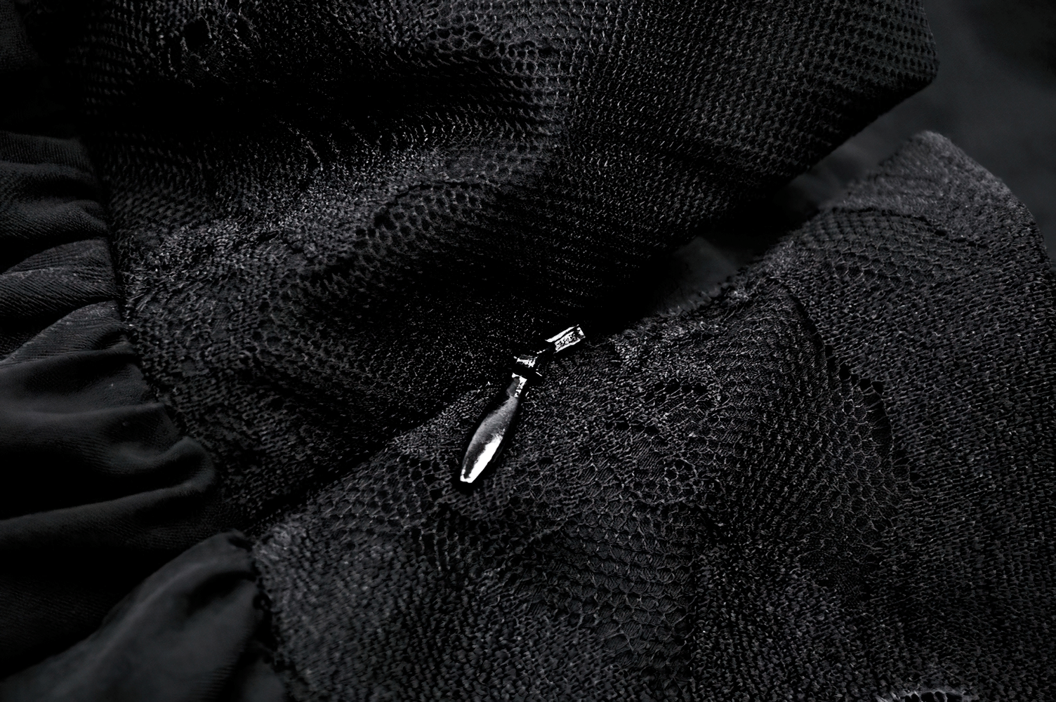 Close-up of intricate black lace fabric with a zipper detail, emphasizing elegance and gothic style in the design.