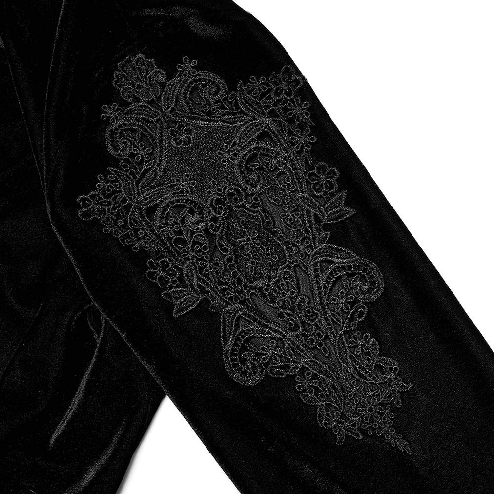 Close-up of embroidered lace detail on the sleeve of an elegant black velvet midi dress.