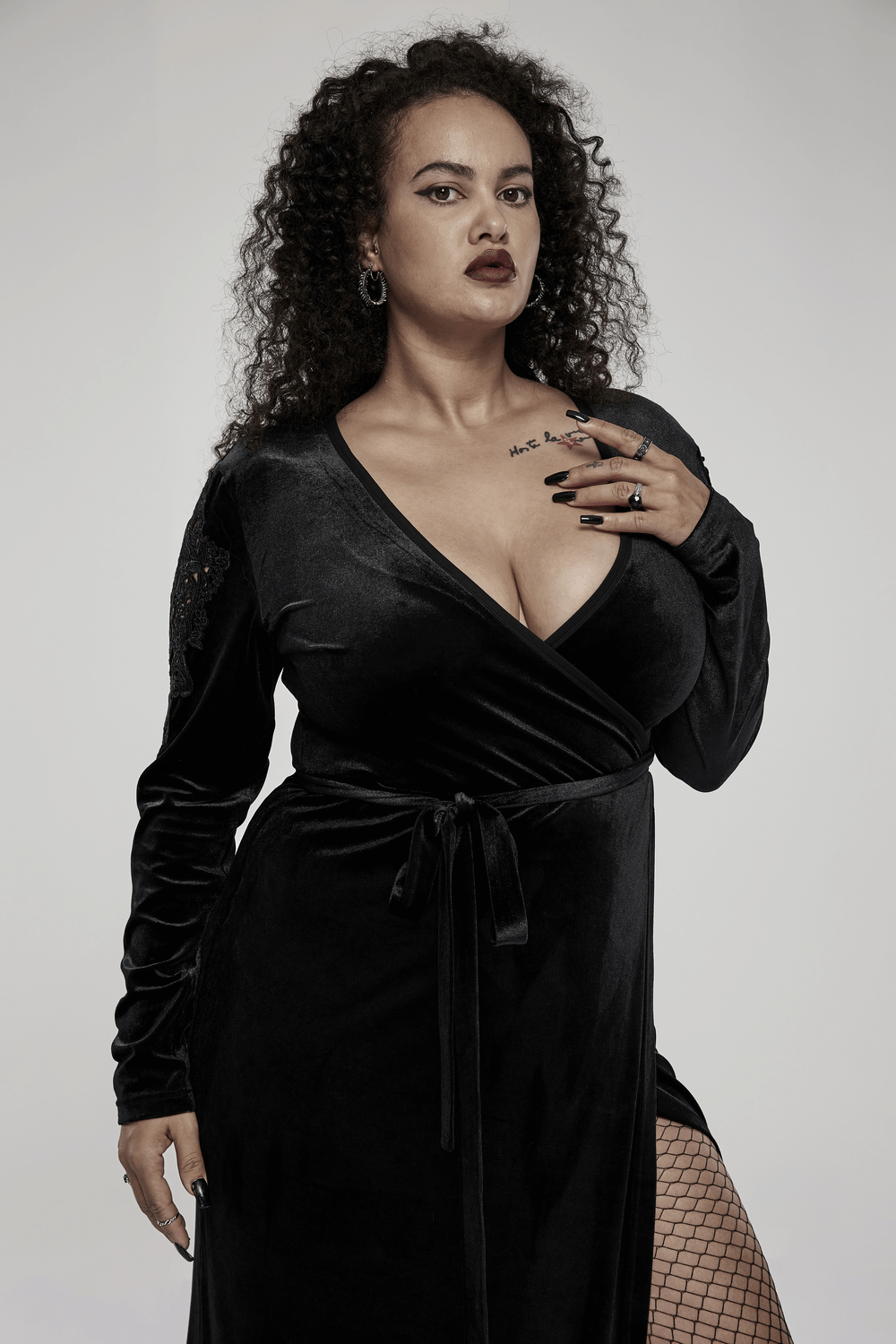 Chic goth model in elegant black velvet midi dress with lace sleeves, showcasing a dramatic V-neck and side slit.