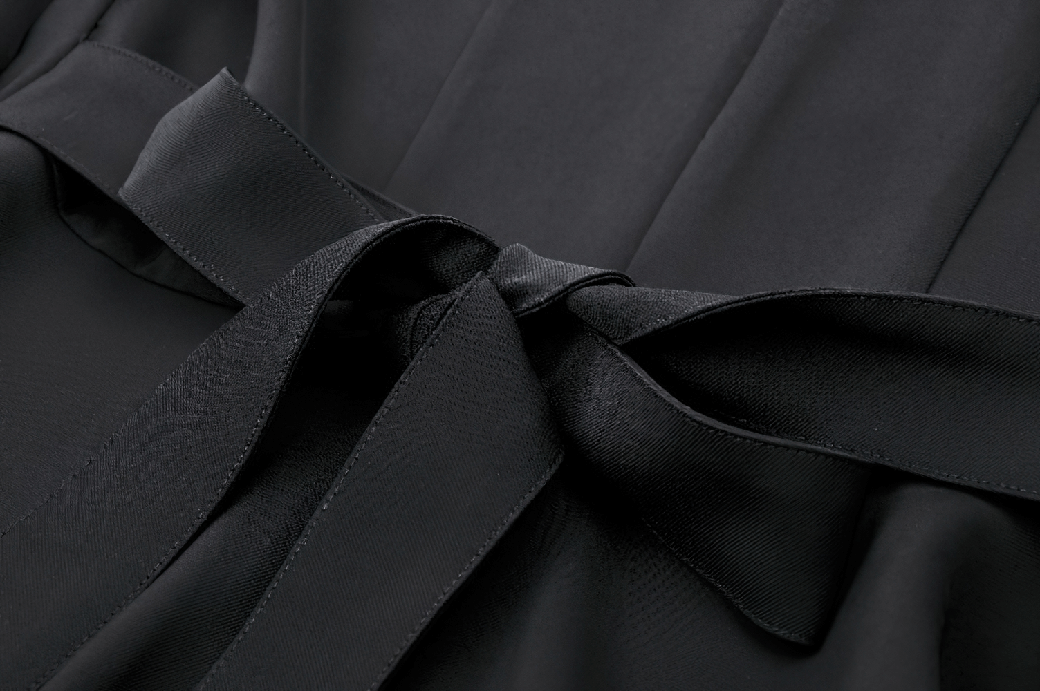 Close-up of a chic black dress featuring a stylish bow detail on the waist, highlighting elegance and sophistication.