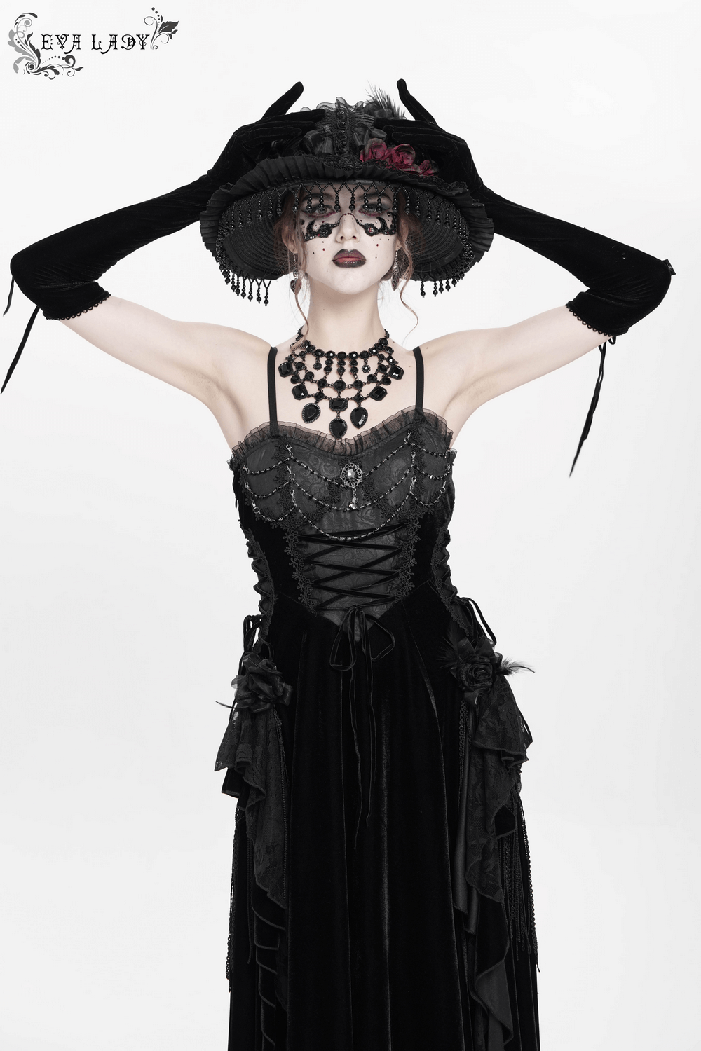 Elegant maxi dress with lace corset and beaded detail, styled with dramatic accessories and a striking hat.