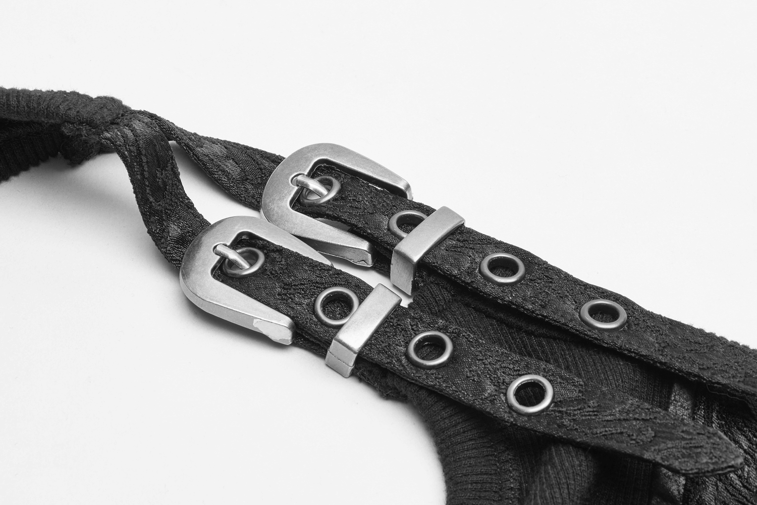 Close-up of black harness straps with metal buckles and eyelets, showcasing intricate design and industrial style.