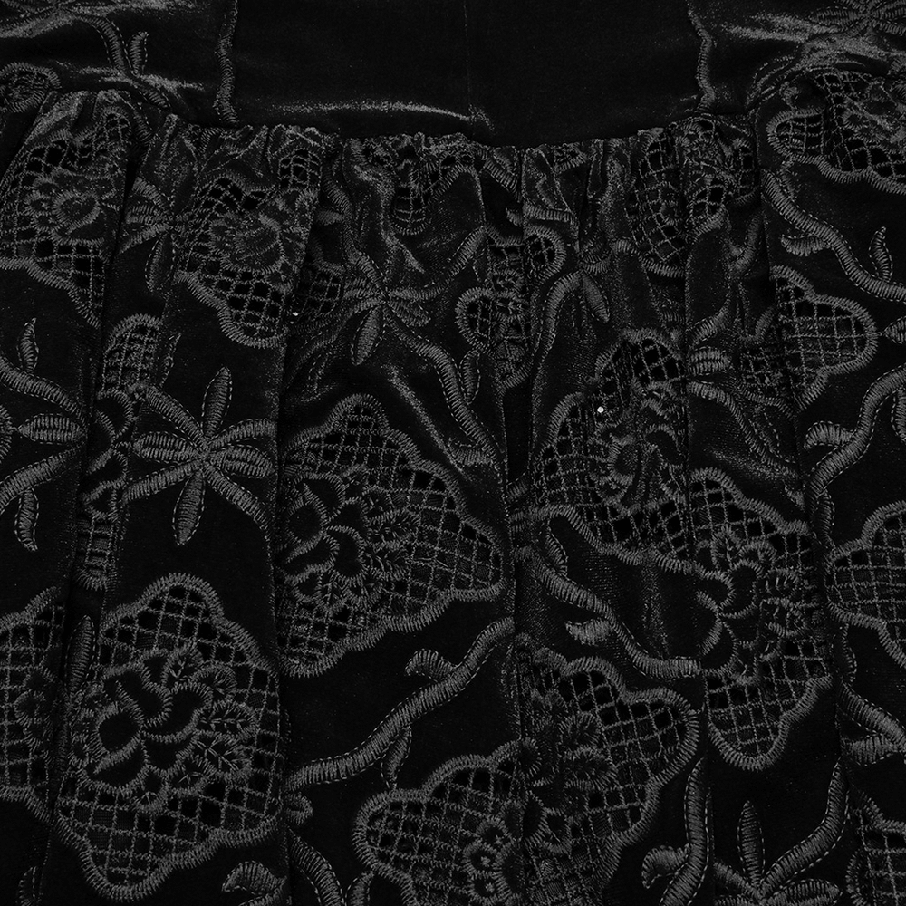 Close-up of elegant velvet fabric with intricate black embroidery and pleated hem, showcasing vintage gothic style.