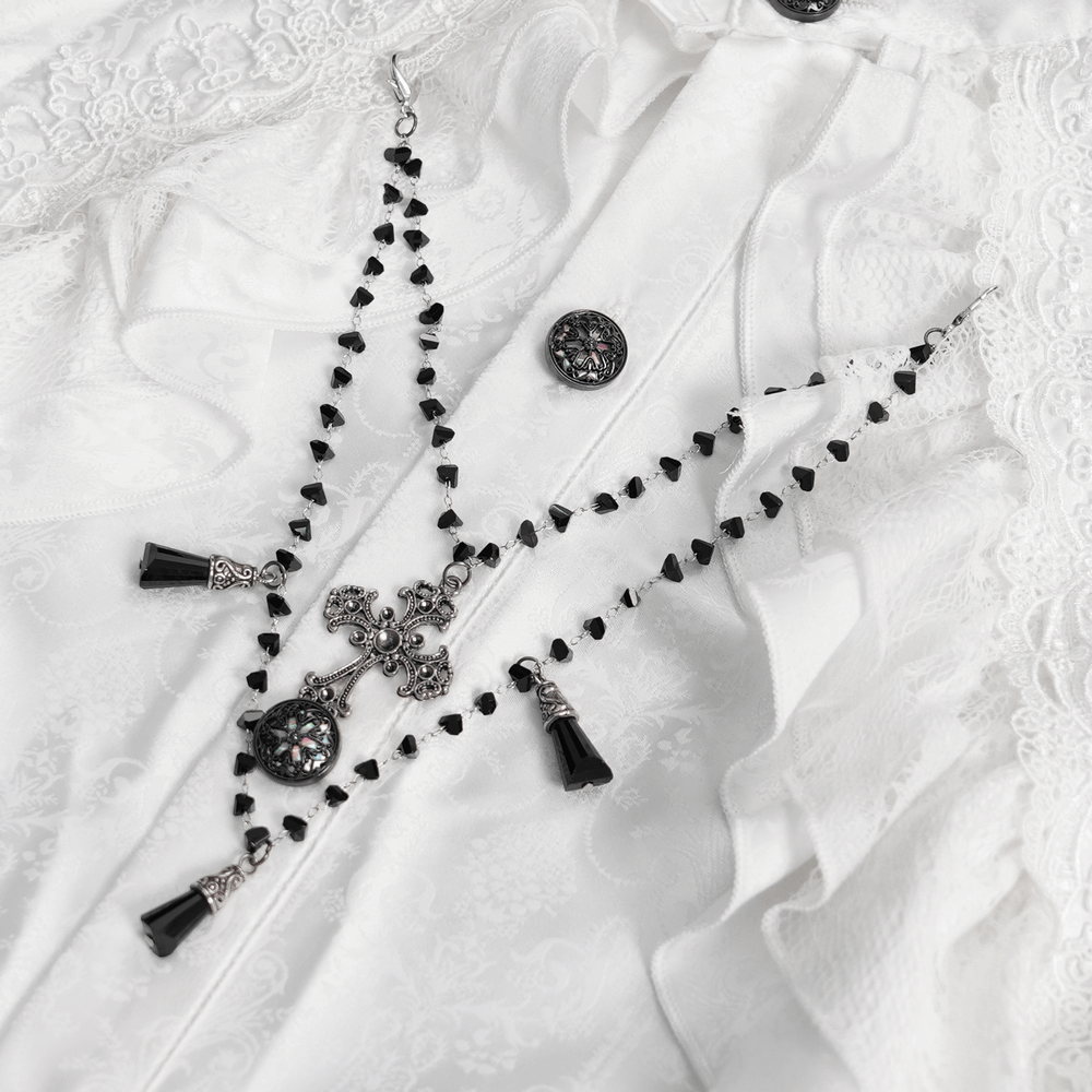 Elegant black and silver necklace with crosses and detailed pendants on a white Victorian ruffled shirt backdrop.