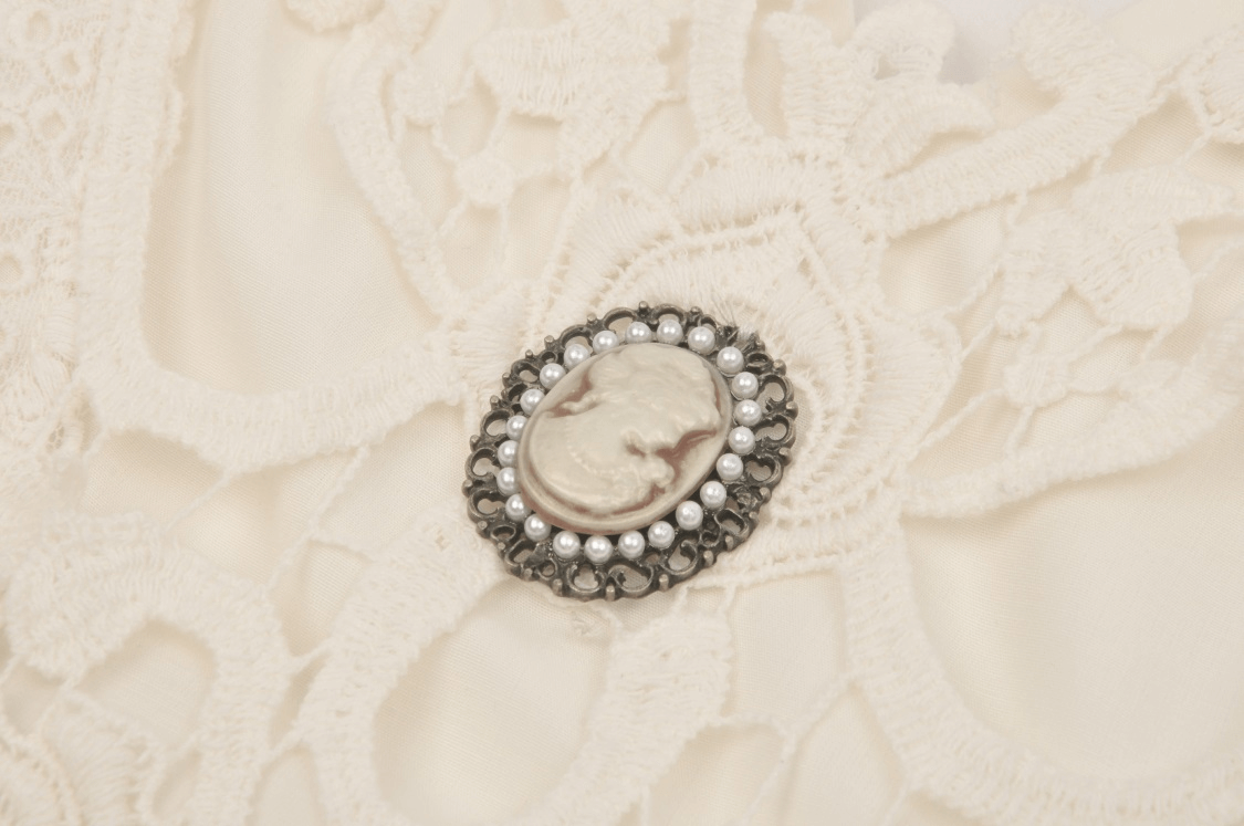 Vintage cameo brooch on intricate lace fabric, adding elegance to the luxurious cream gown.