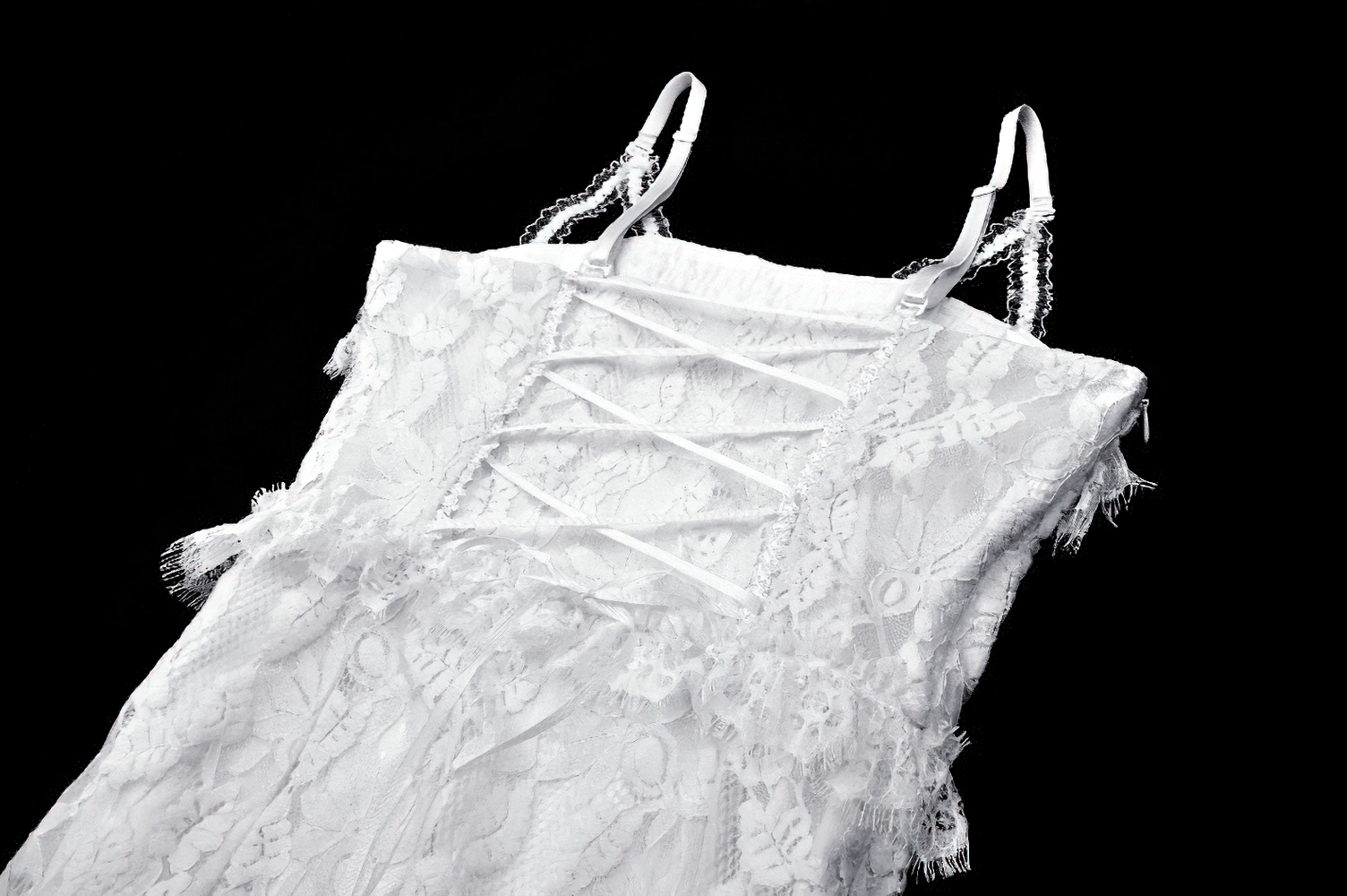 Elegant white lace mermaid dress with spaghetti straps and ruffled details against a dark background.