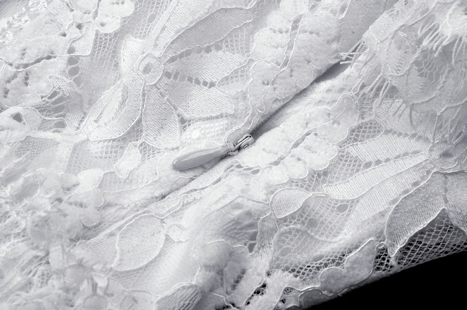 close-up of elegant white lace fabric with intricate details and zipper, showcasing ruffled texture and delicate design elements.