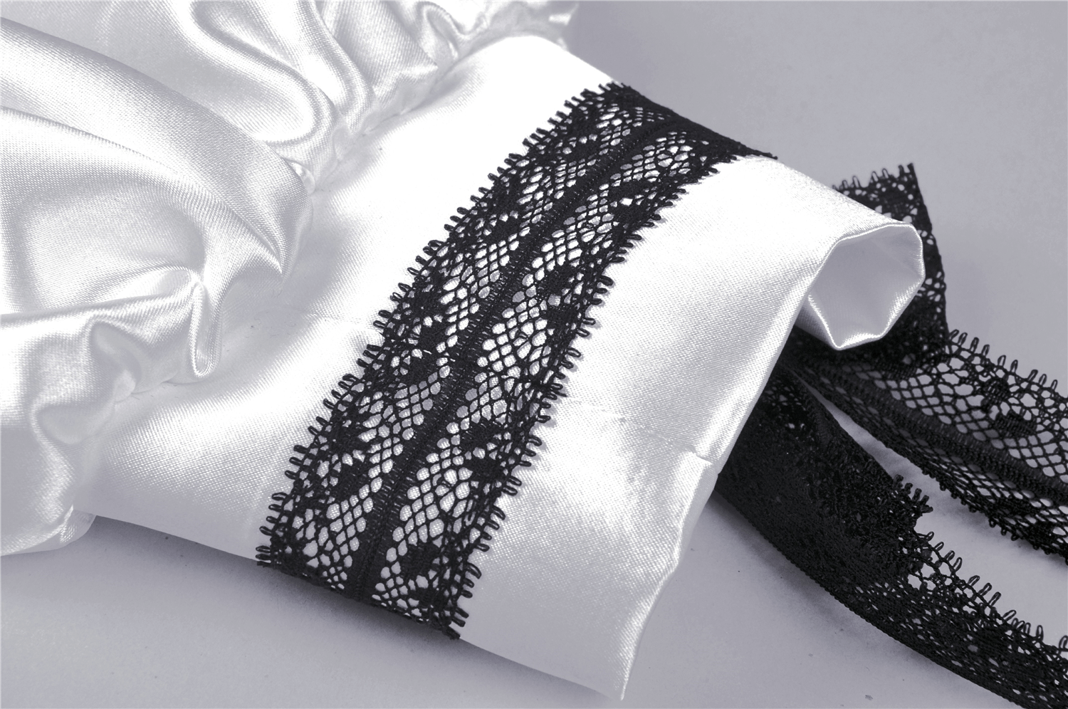 Close-up of elegant white satin fabric with intricate black lace detailing for a stylish dress.