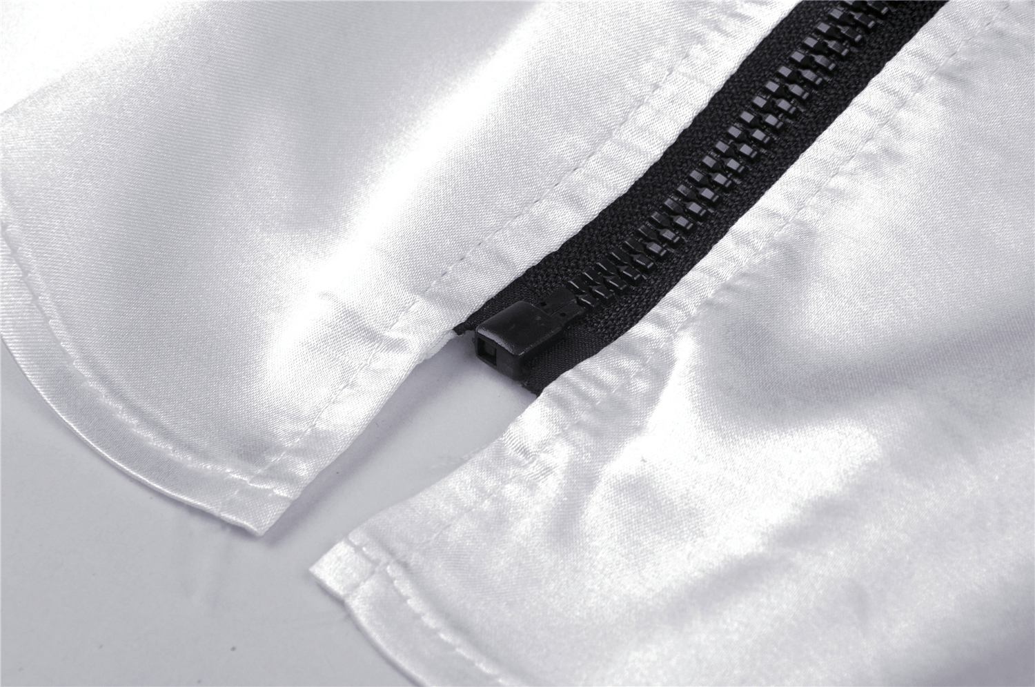 Close-up of elegant white satin fabric with a sleek black zipper detail, showcasing quality and style.