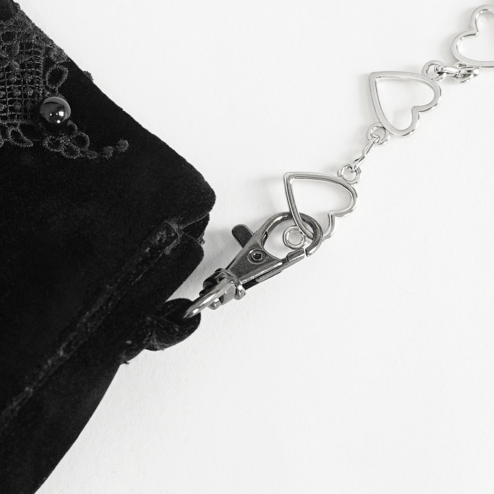 Close-up of the silver heart chain strap on an elegant black velvet shoulder bag with embroidered details.