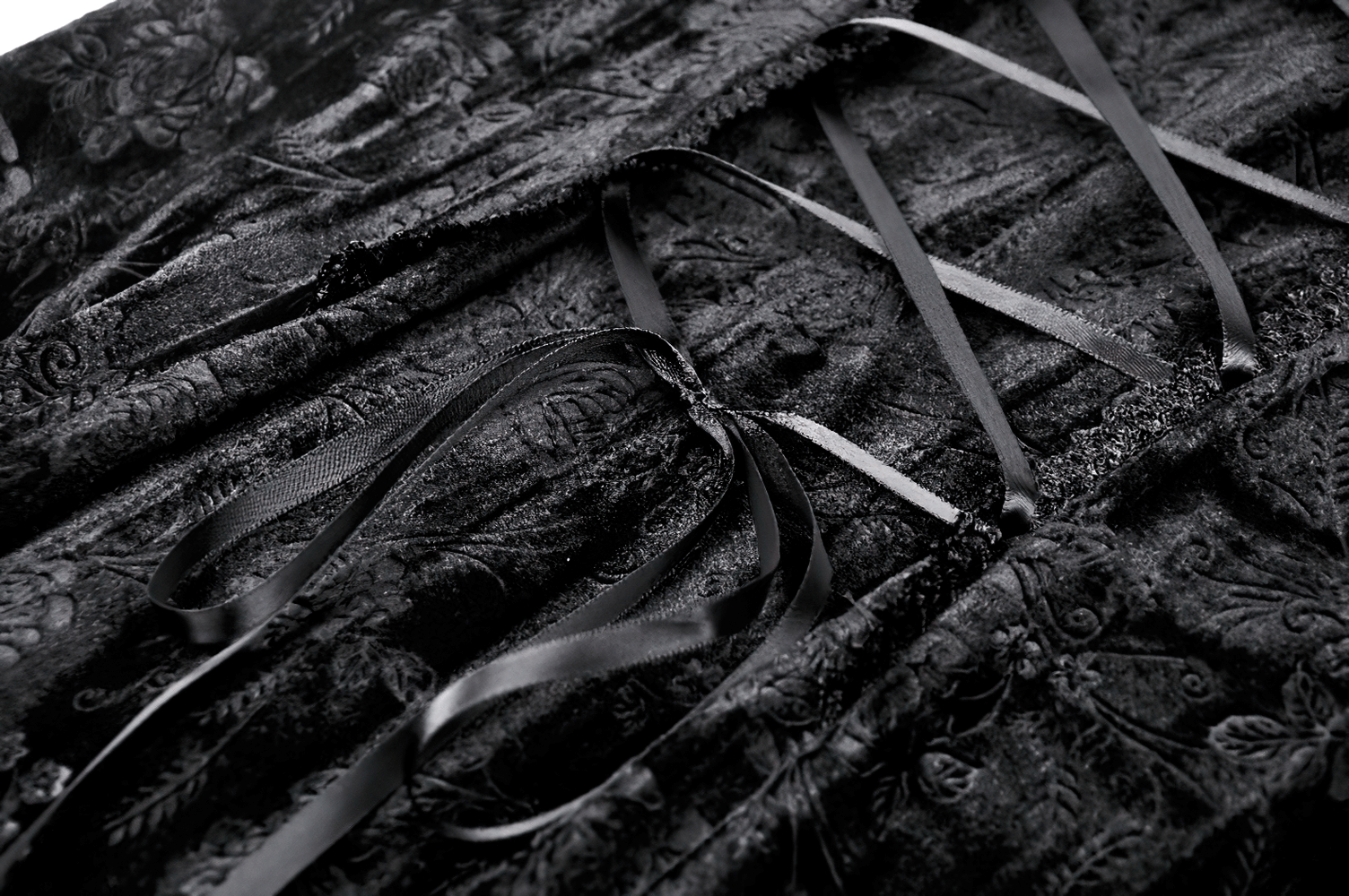Close-up of intricate black velvet dress with lace and satin ribbons showcasing elegant gothic details.