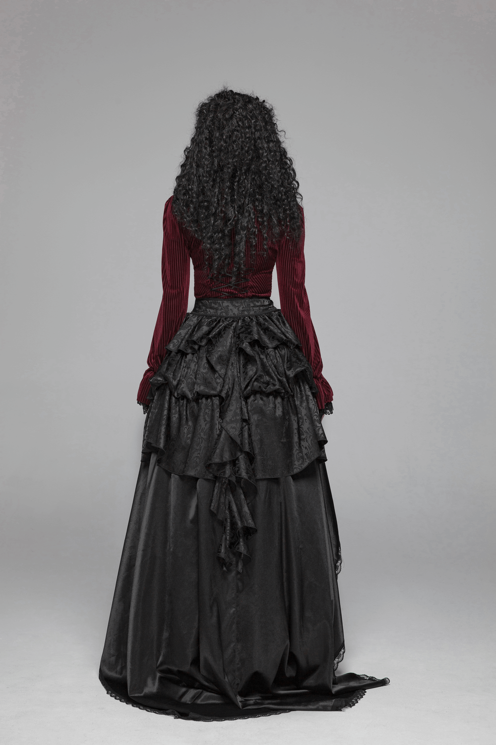 Back view of a model in a burgundy velvet corset shirt paired with a black ruffled skirt, showcasing gothic style elegance.