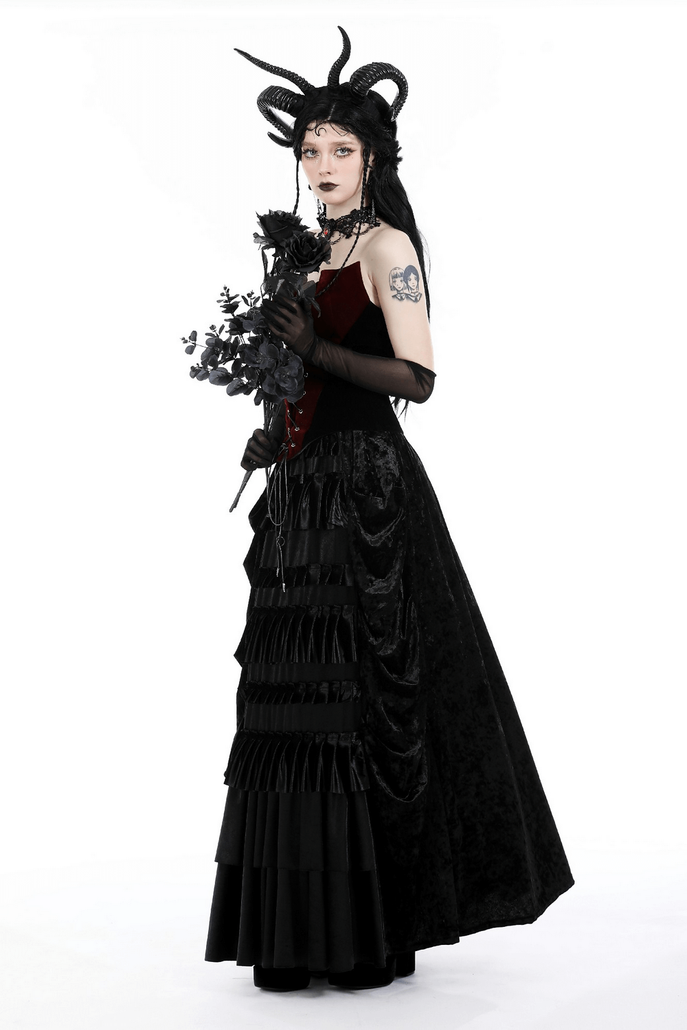 Elegant woman in a dramatic black velvet corset and long skirt, styled with horns and holding dark flowers.