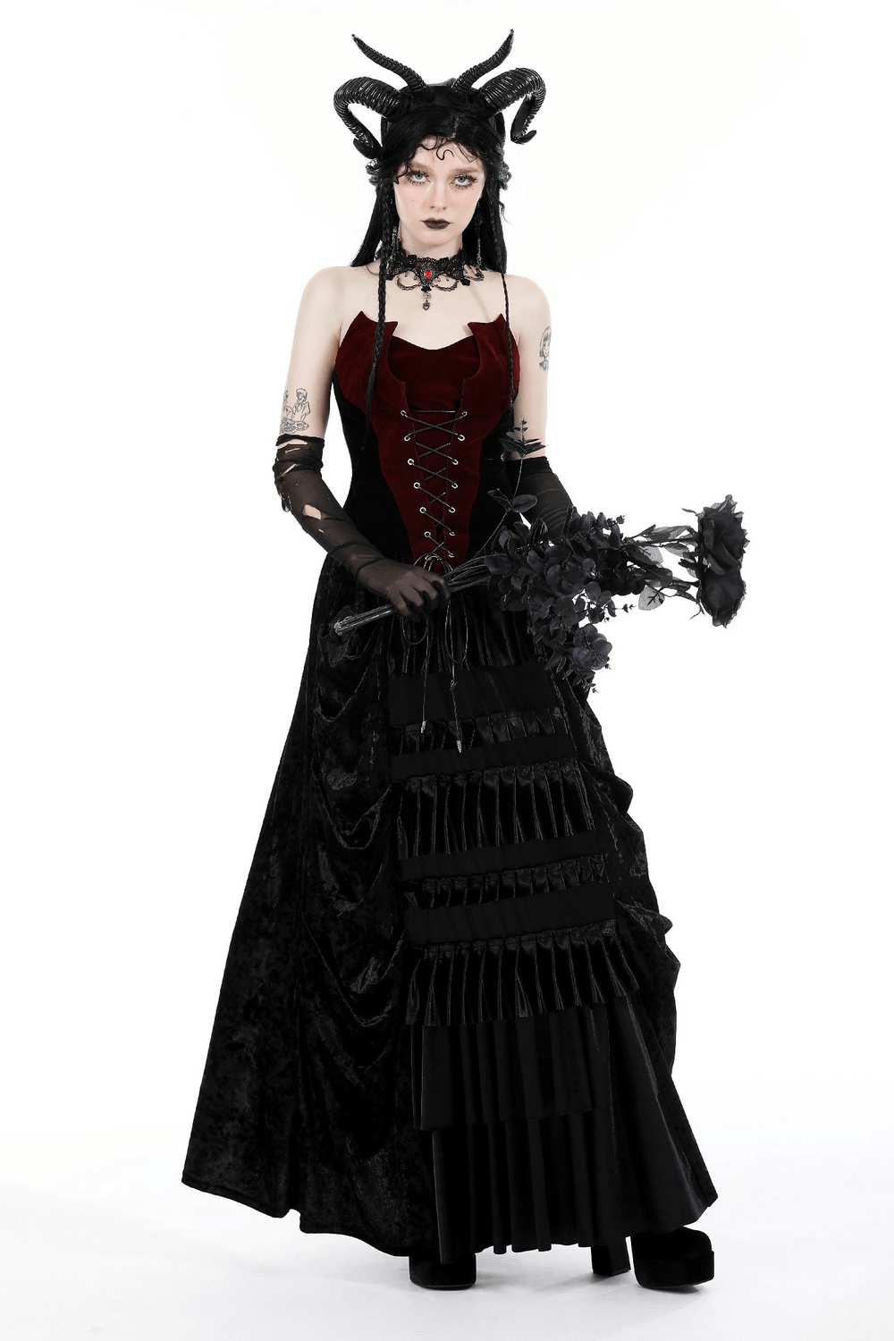 Elegant woman in a wine-red velvet corset with lace-up front, paired with a dramatic black skirt and holding black flowers.