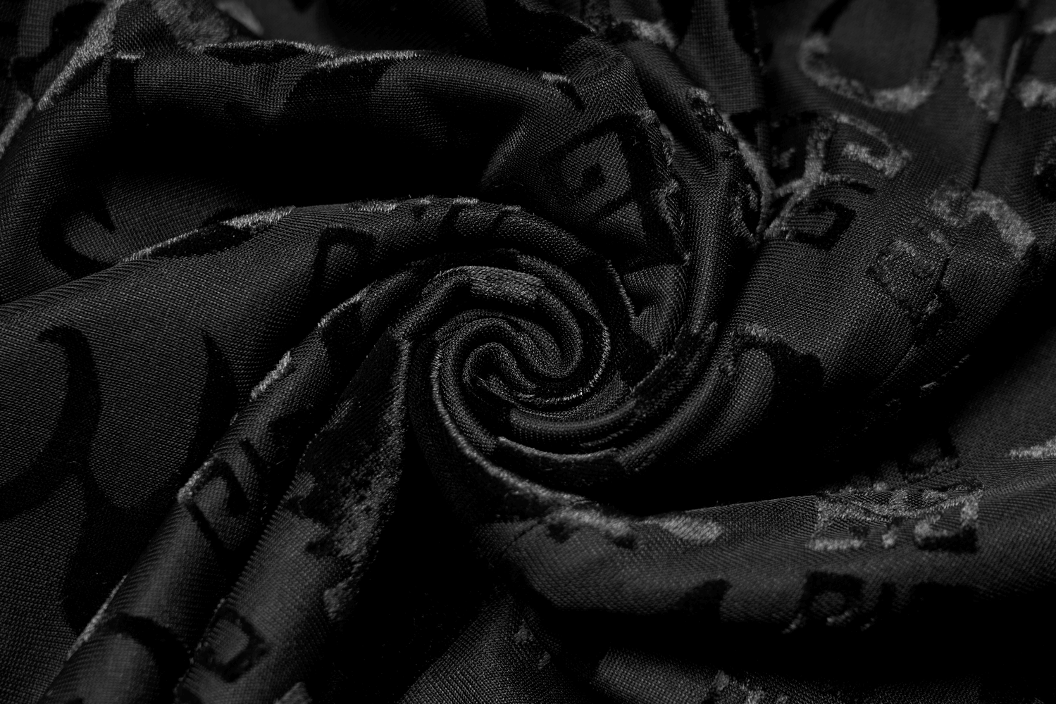Close-up of luxurious black velvet fabric showcasing intricate dragon pattern swirls, perfect for couture garments.
