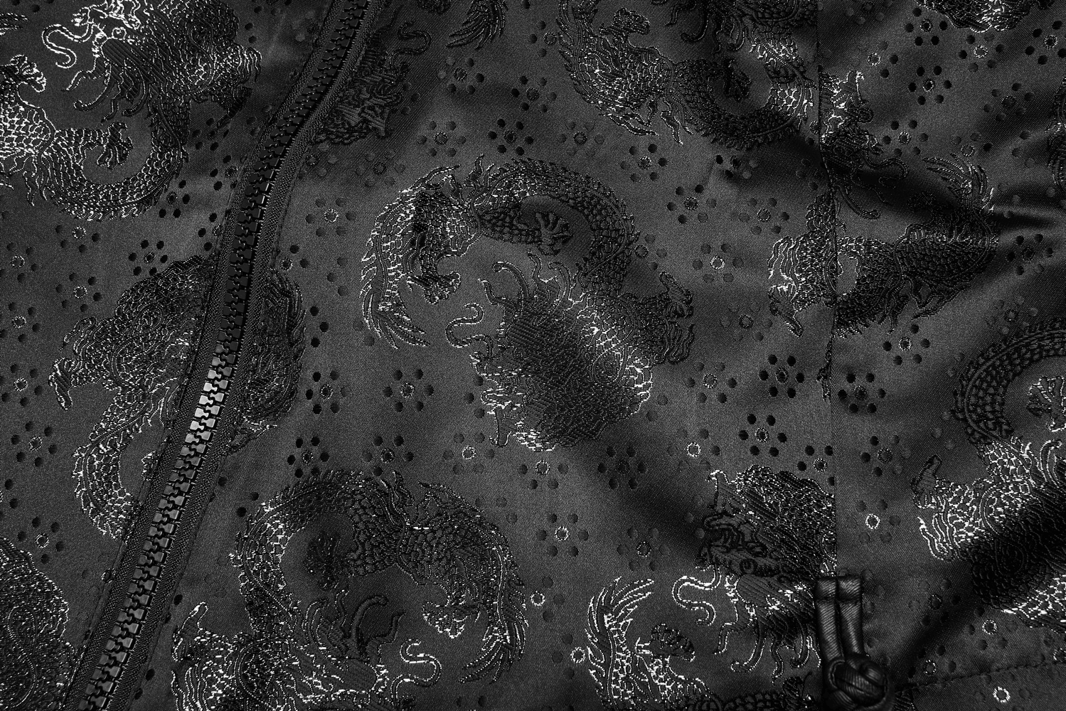 Close-up of an embroidered dragon jacquard pattern on a sleek black fabric skirt.