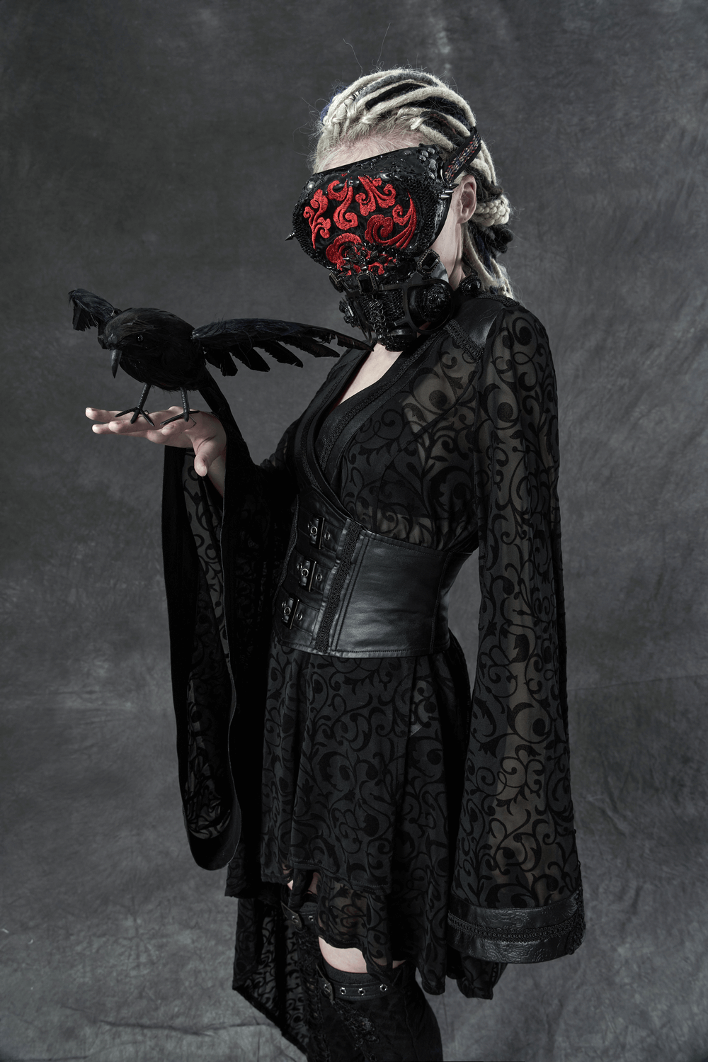 Model in elegant black Gothic kimono dress with intricate embroidery and a striking mask, holding a crow.