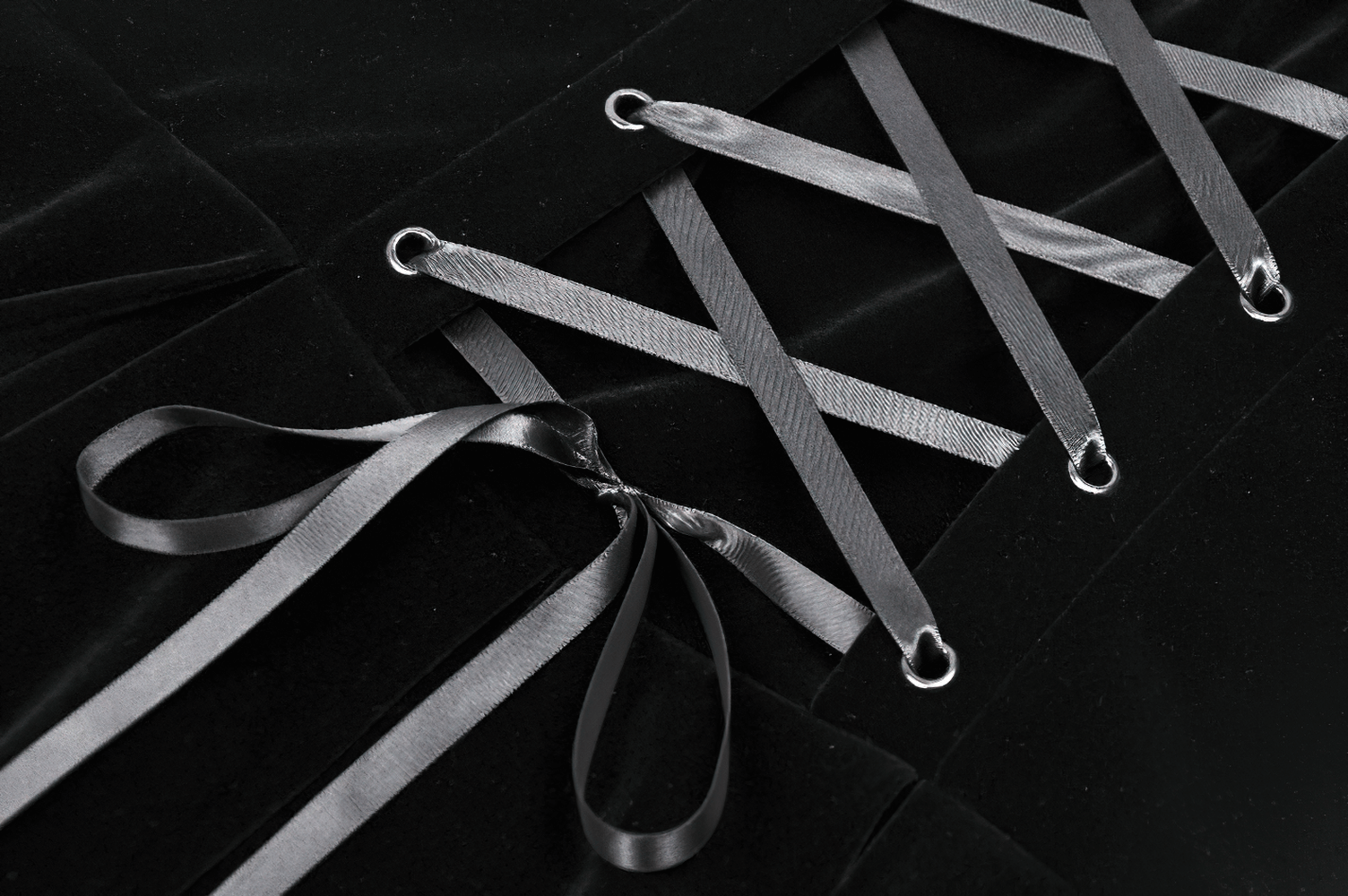 Close-up of the intricate lace-up back of a black velvet Gothic dress with stylish gray satin ribbons.